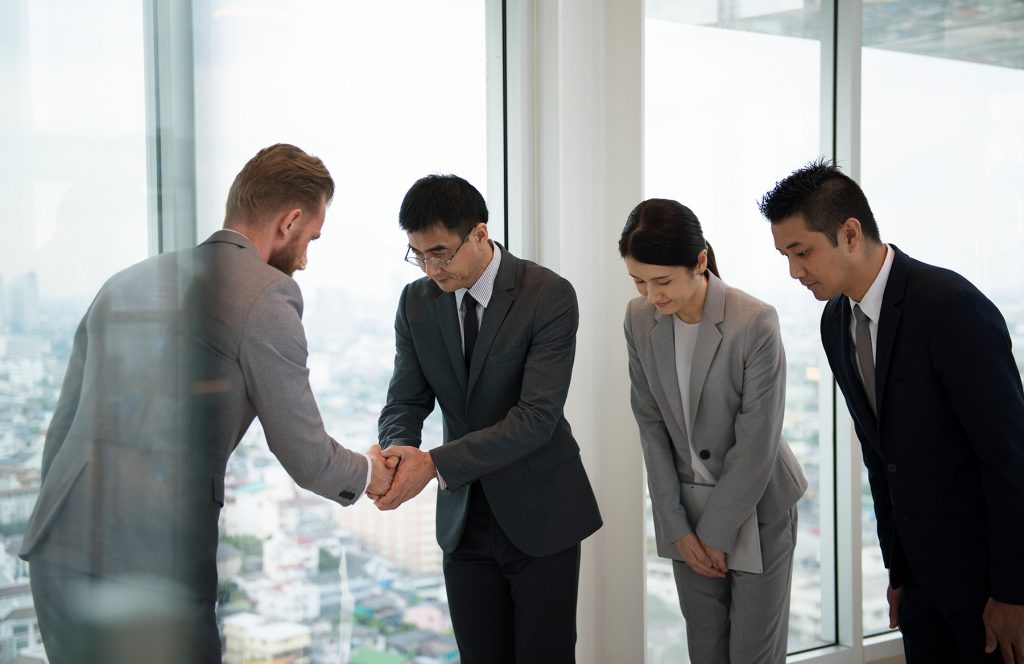 Western and Asian financial employees bowing before discussing equity compensation