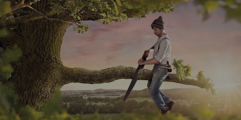 Person sitting on a tree bunch about to cut the branch which will lead to them falling.